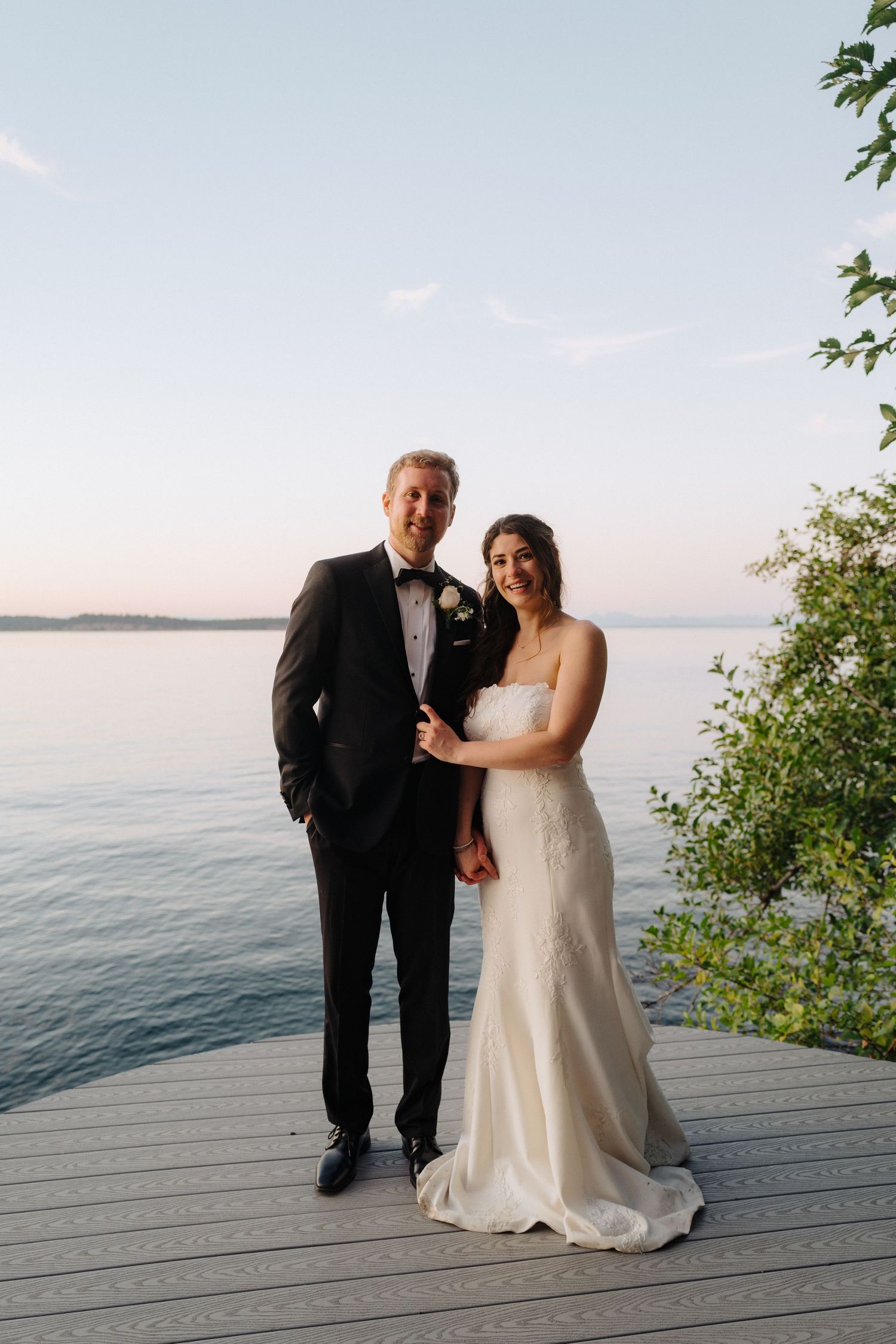 Newlyweds pose for portrait on waterfront deck during golden hour.