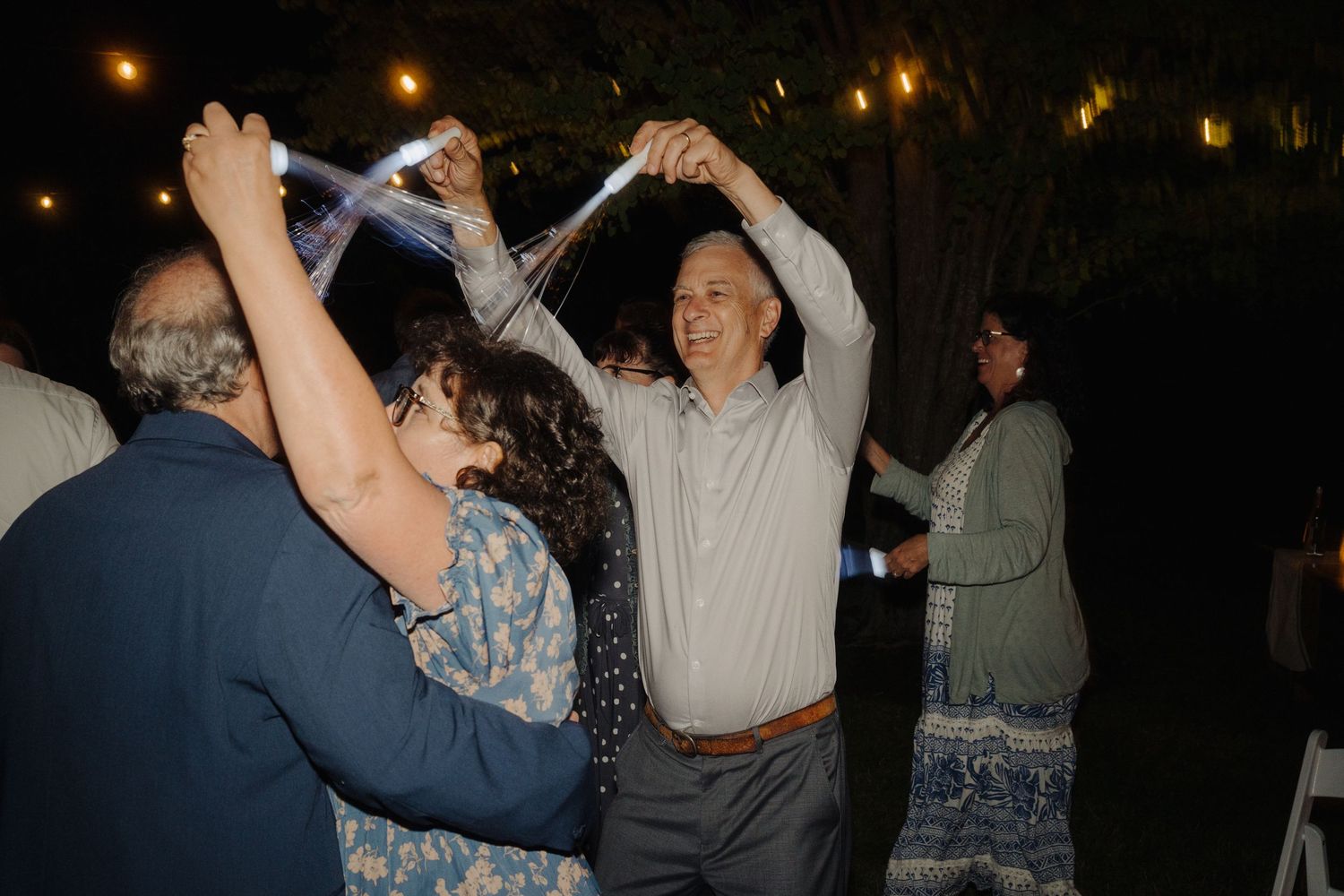 Wedding guests dance joyfully under warm outdoor lighting at an evening reception.