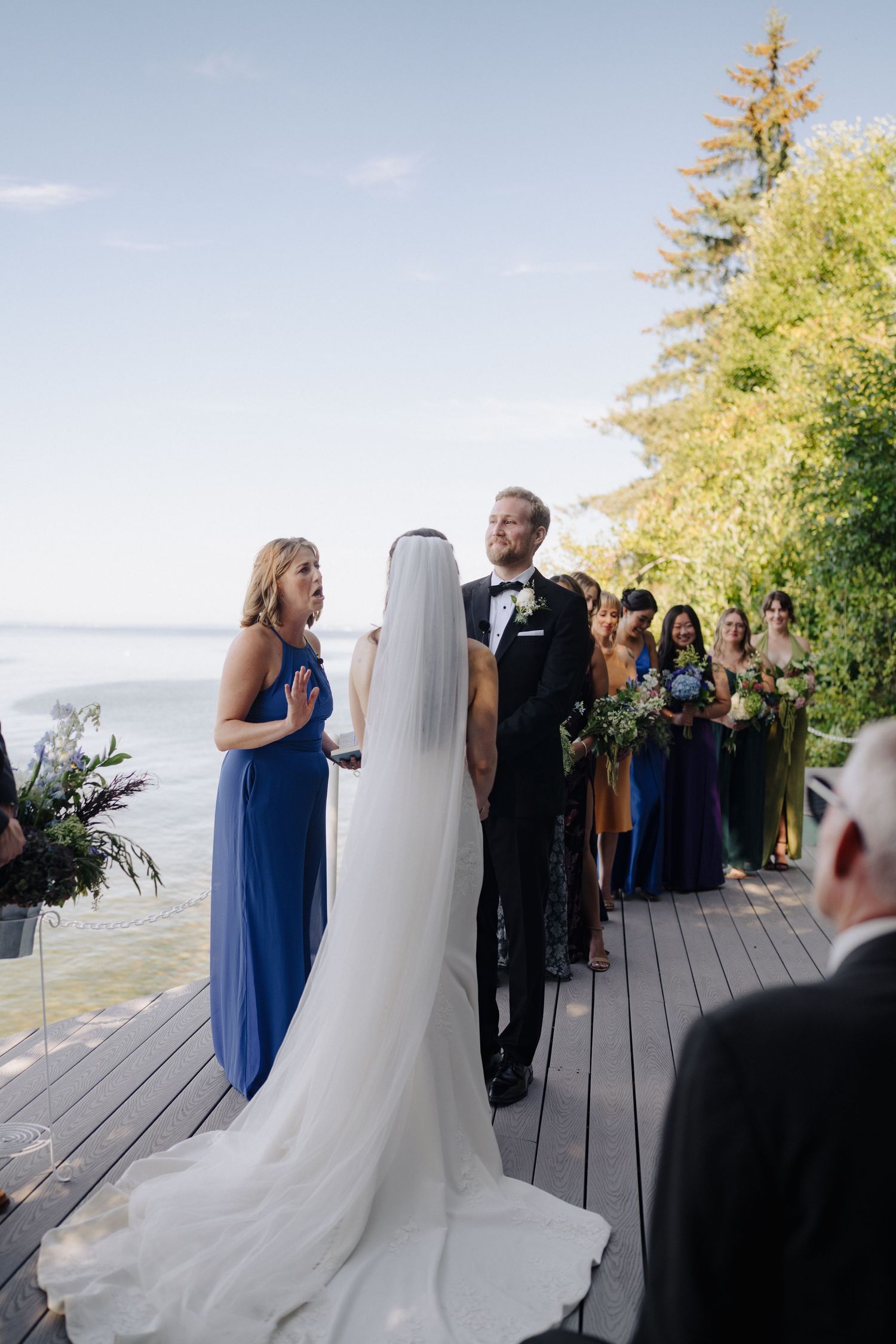 Outdoor wedding ceremony on a waterfront deck with attendants in formal attire.
