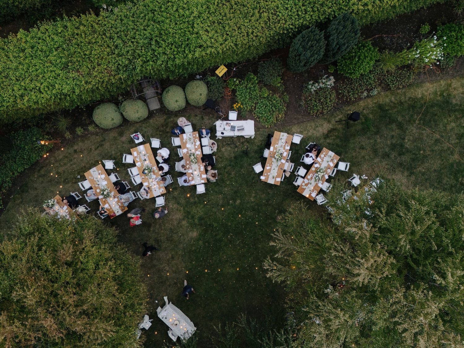 Aerial view of outdoor wedding reception tables and guests in a lush garden setting.