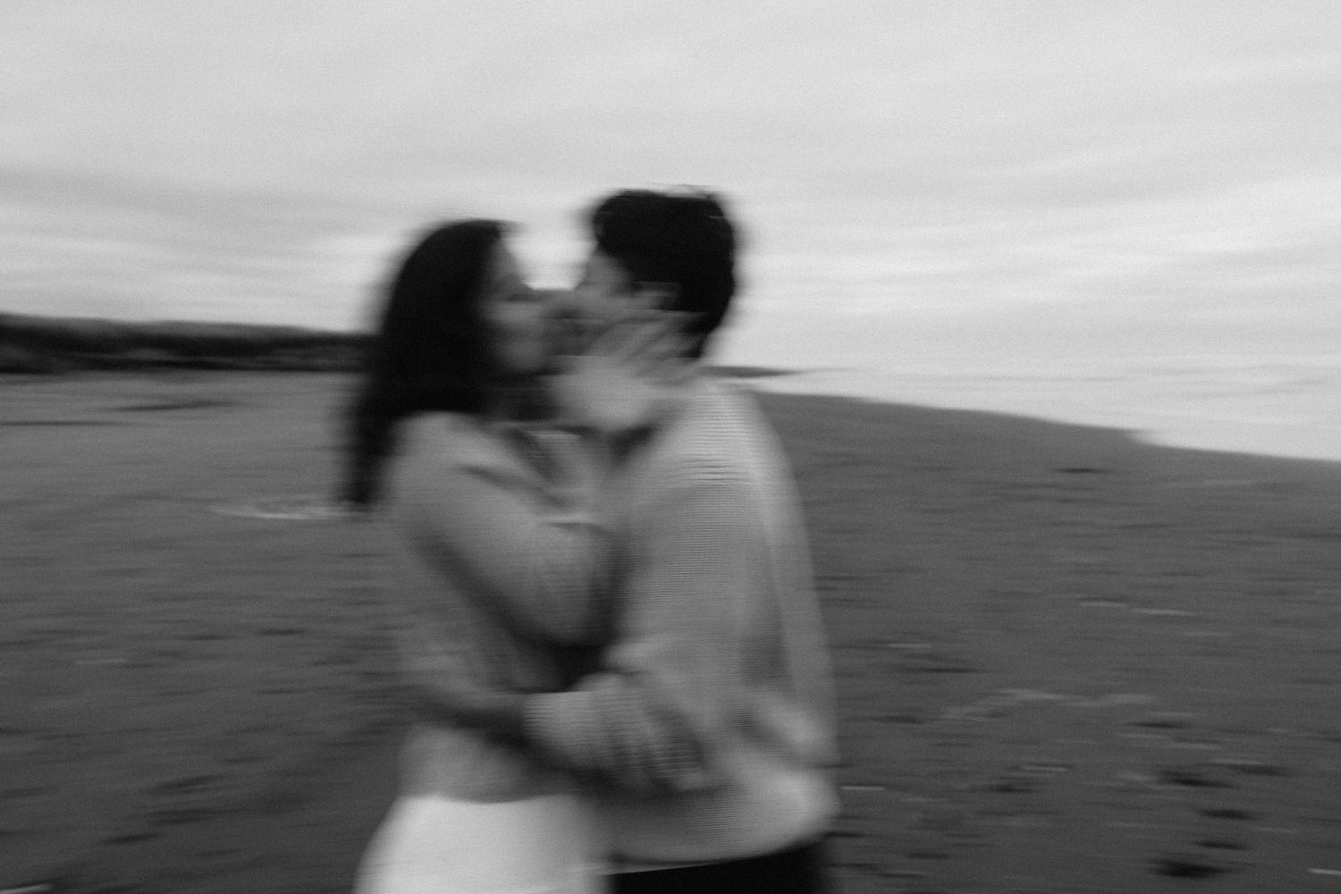 Blurred black and white photo of couple sharing a passionate kiss by the ocean.