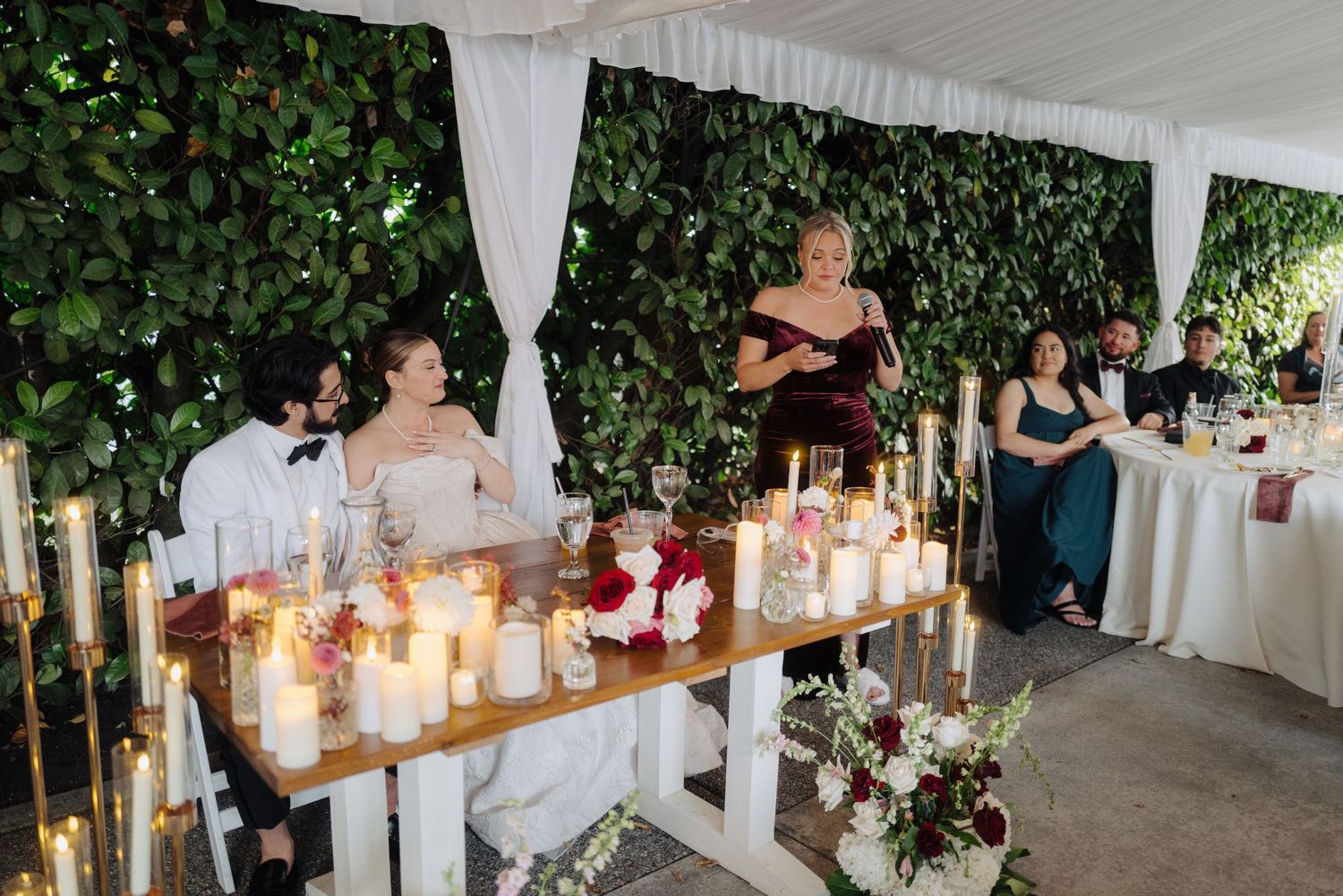 Wedding reception table decorated with candles and floral arrangements against a green wall.