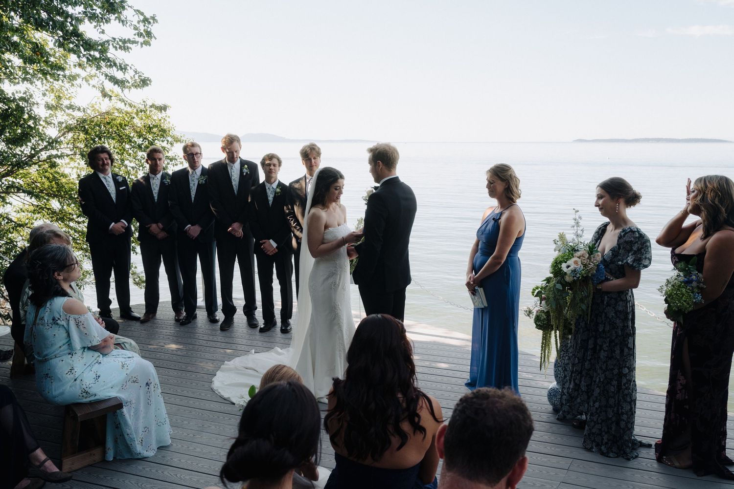 Intimate waterfront wedding ceremony with guests gathered on a wooden deck.