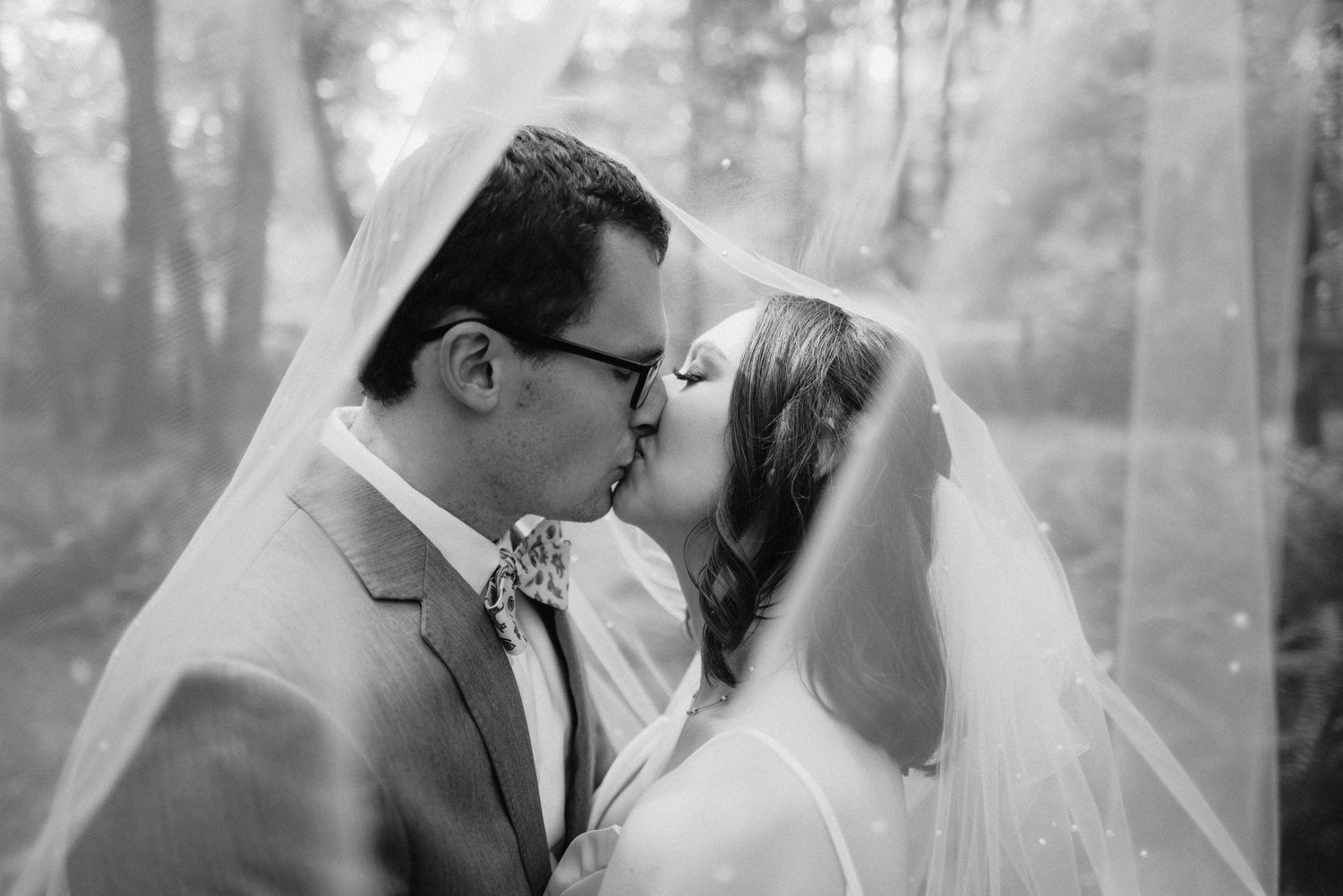 Black and white romantic wedding portraits captured in a misty forest setting.