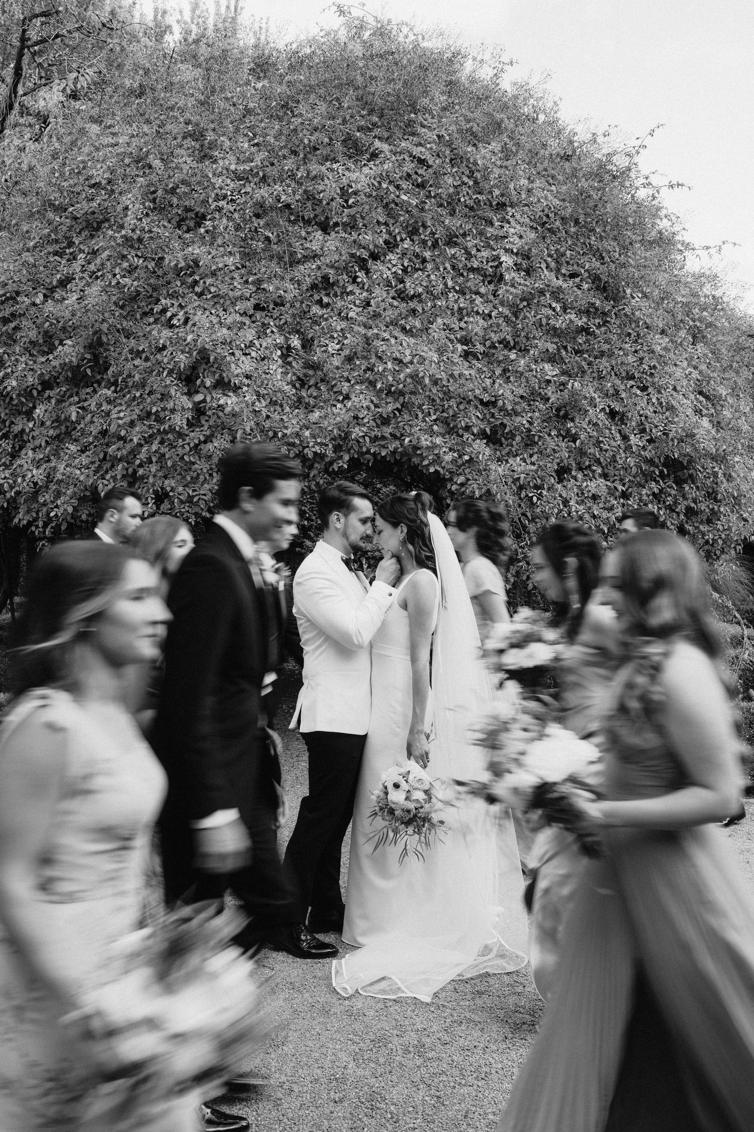 Wedding guests dance and celebrate in a joyful motion blur under trees at an outdoor reception.