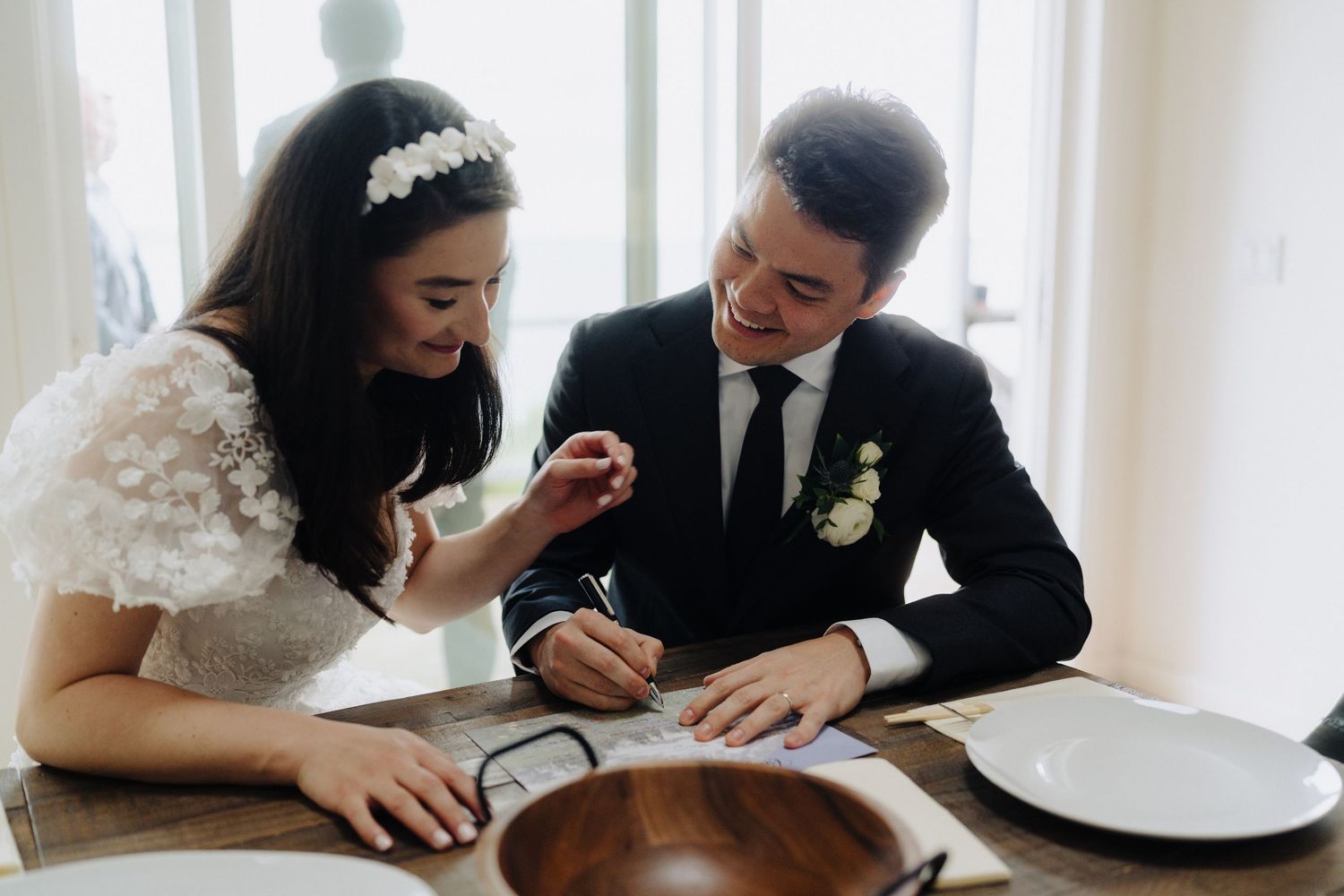 A couple signing their marriage license together at a bright indoor venue.
