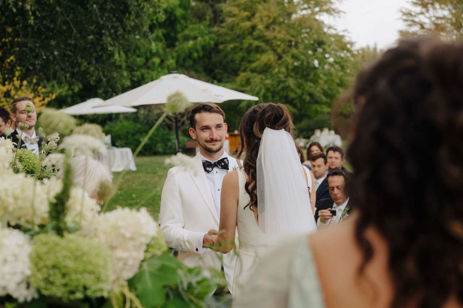 Outdoor summer wedding ceremony with white floral decor and garden setting.