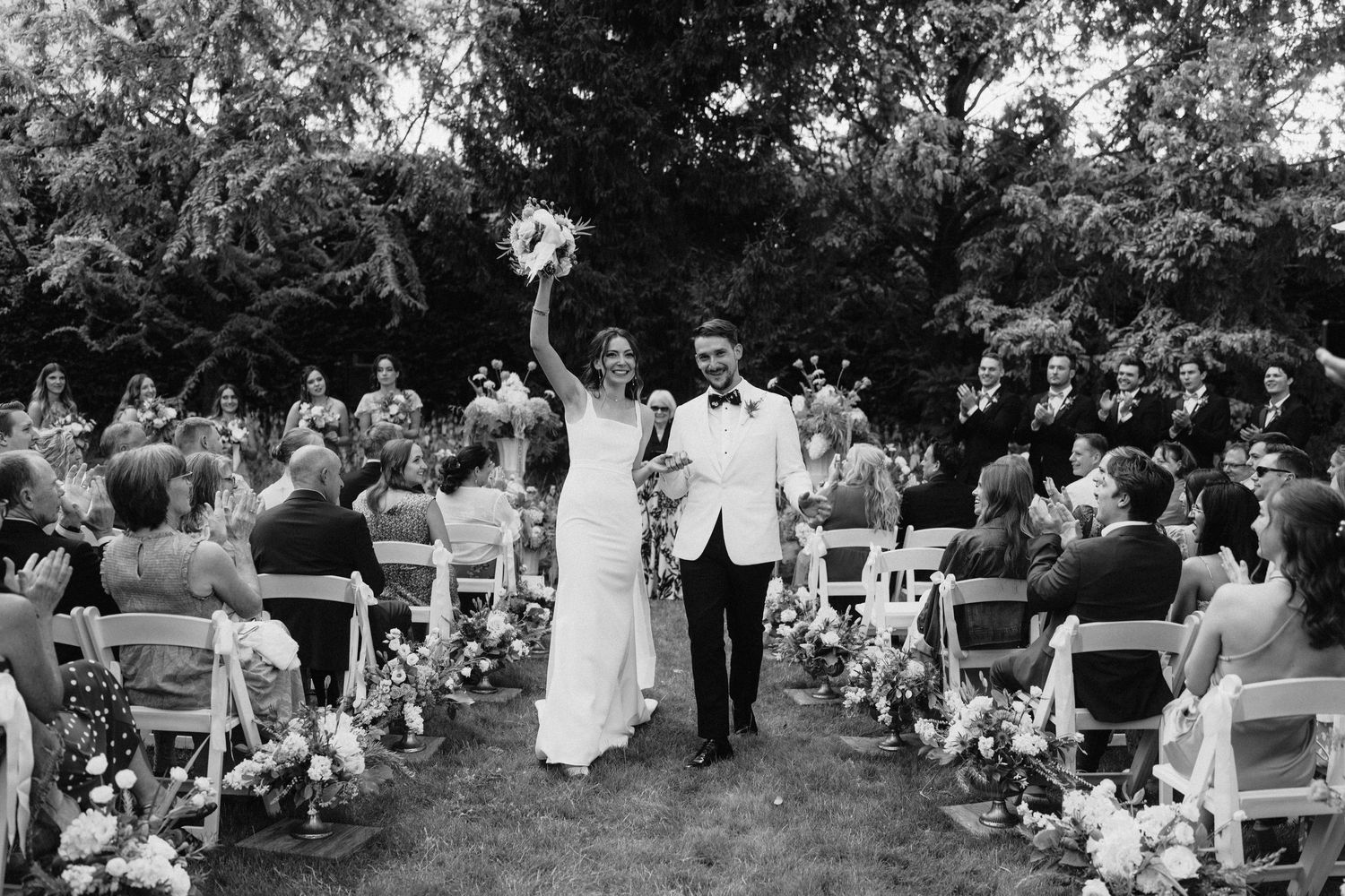 Black and white photograph of wedding guests seated in rows during an outdoor ceremony.