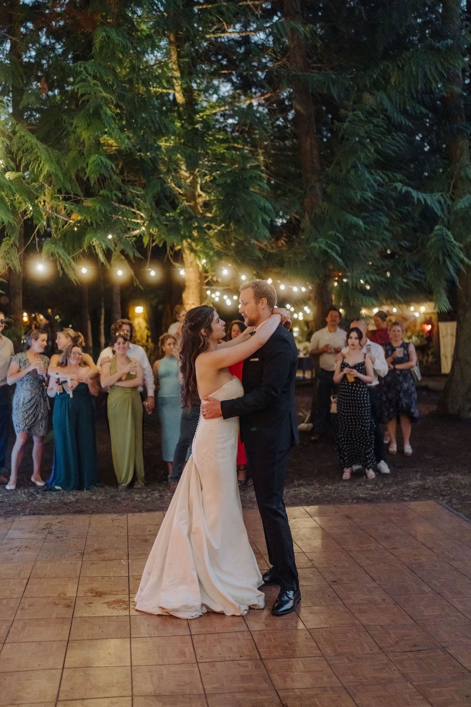 Wedding couples dance together on an outdoor patio under string lights at dusk.