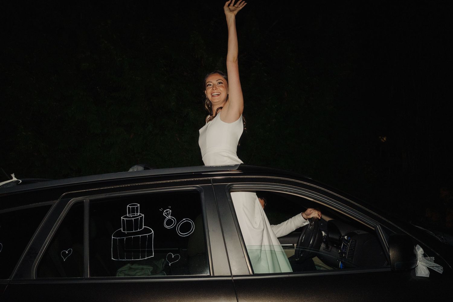 Bride waving from car window during nighttime wedding departure.