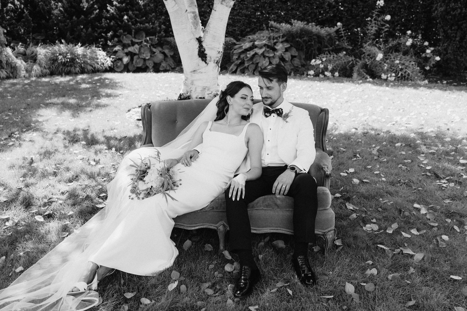 Black and white photo of a couple relaxing on grass during their wedding day.
