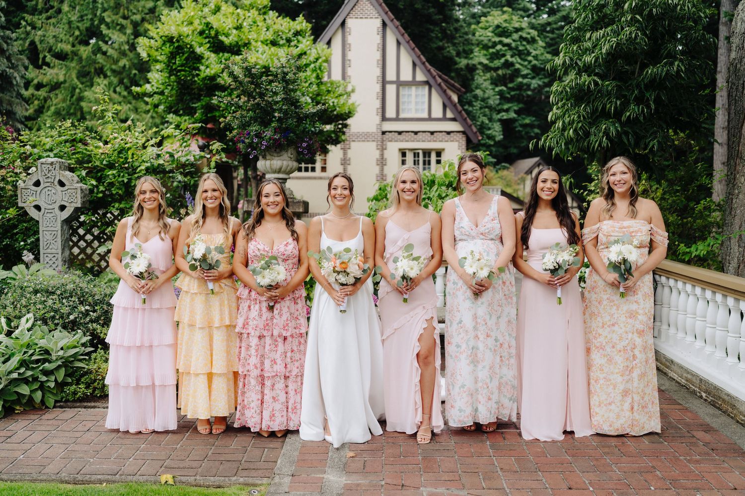 Bridesmaids in pastel pink dresses pose together outdoors at an elegant garden wedding venue.