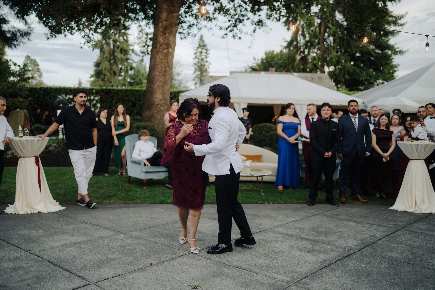 Wedding guests dancing and celebrating on outdoor patio under string lights.