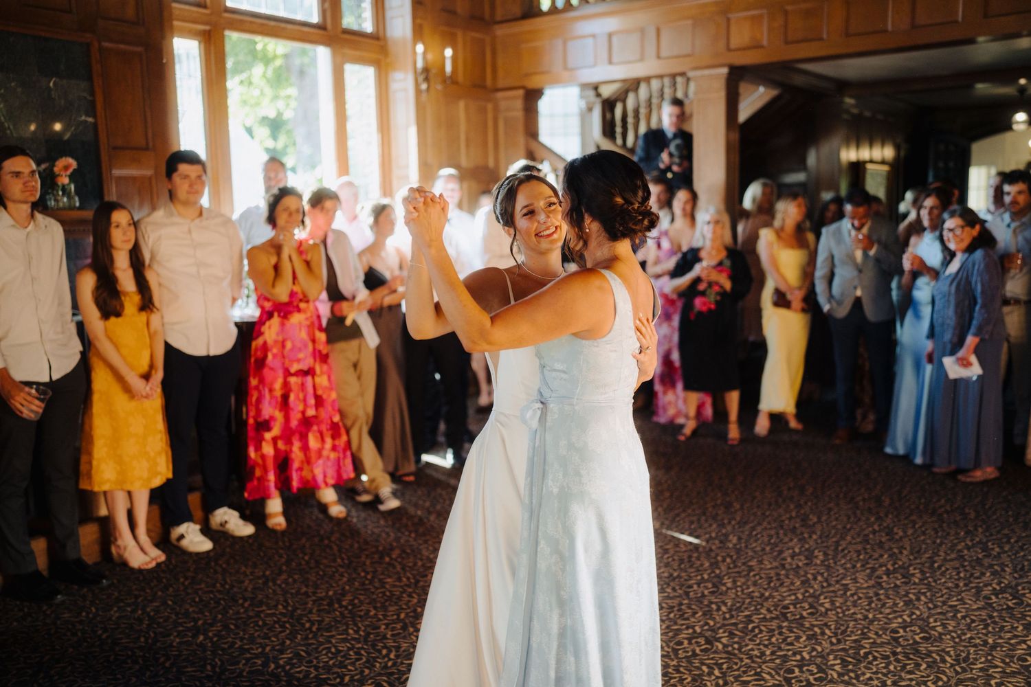 Wedding party dances in an elegant wood-paneled reception hall with guests watching.
