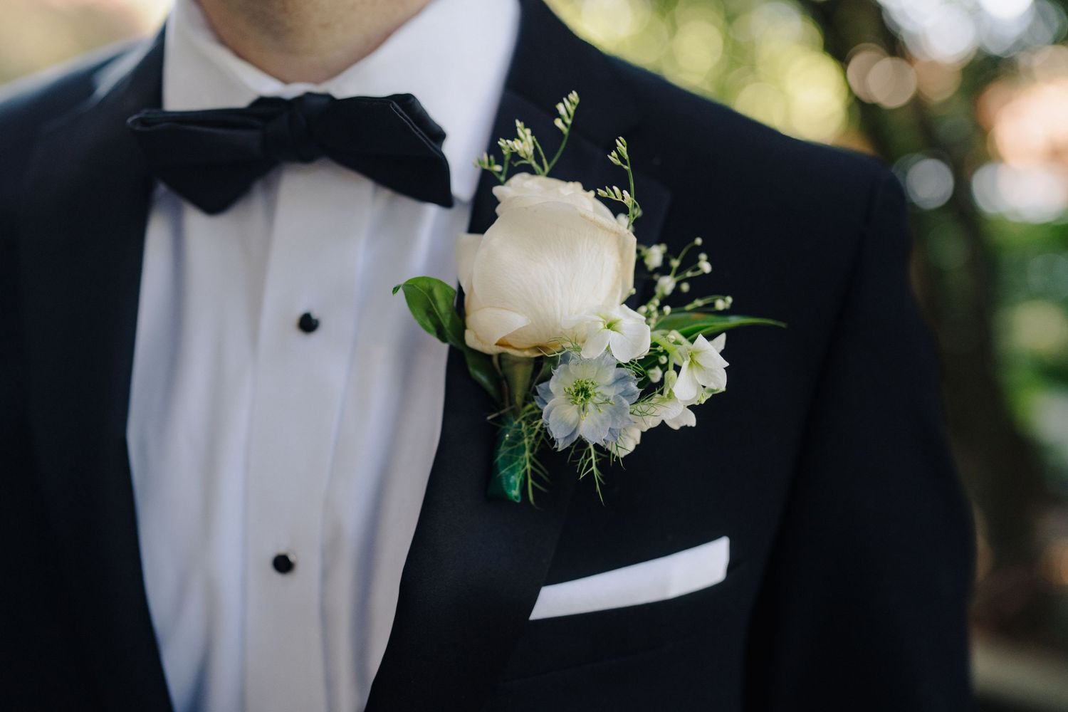 Formal wedding attire detail showing black tuxedo jacket with white boutonniere flower pinned to lapel.