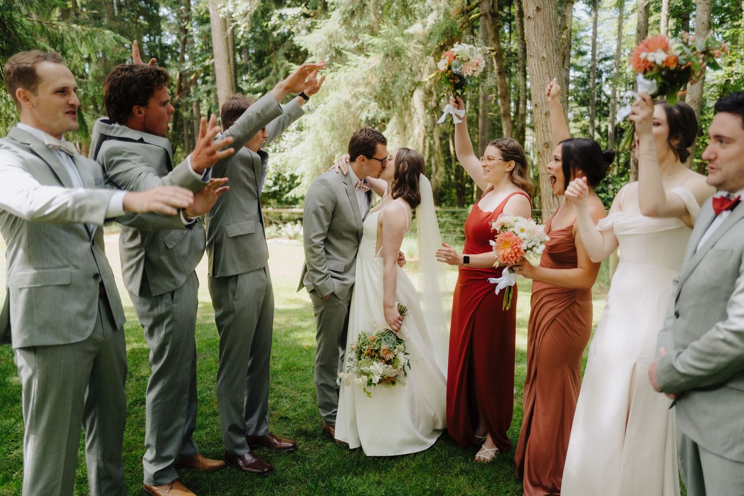 Wedding celebration with bridal party in grey suits and burgundy dresses outdoors.