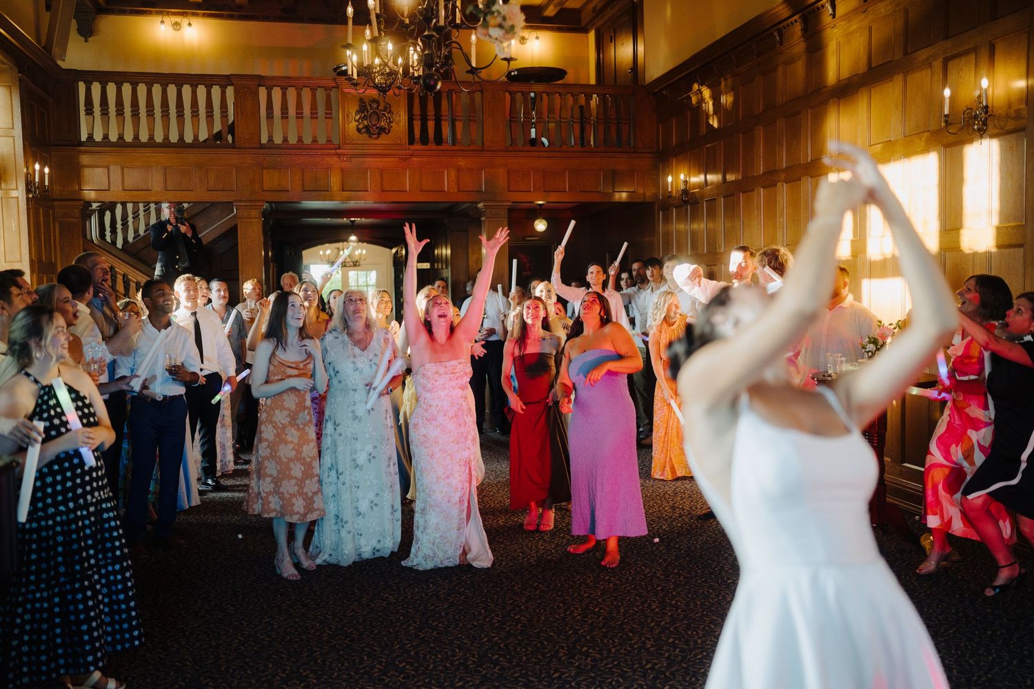 Wedding reception guests dancing and celebrating in a rustic barn venue with chandeliers.