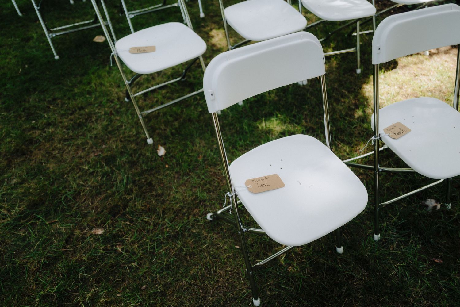 White folding chairs arranged outdoors for a wedding ceremony in a wooded setting.