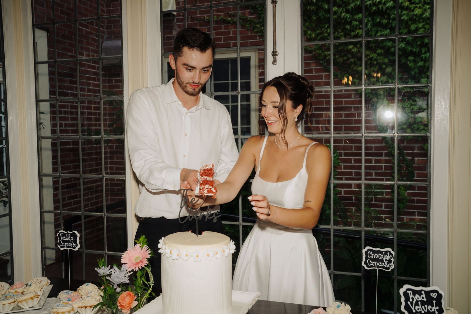 Couple cuts their wedding cake together in elegant indoor setting.