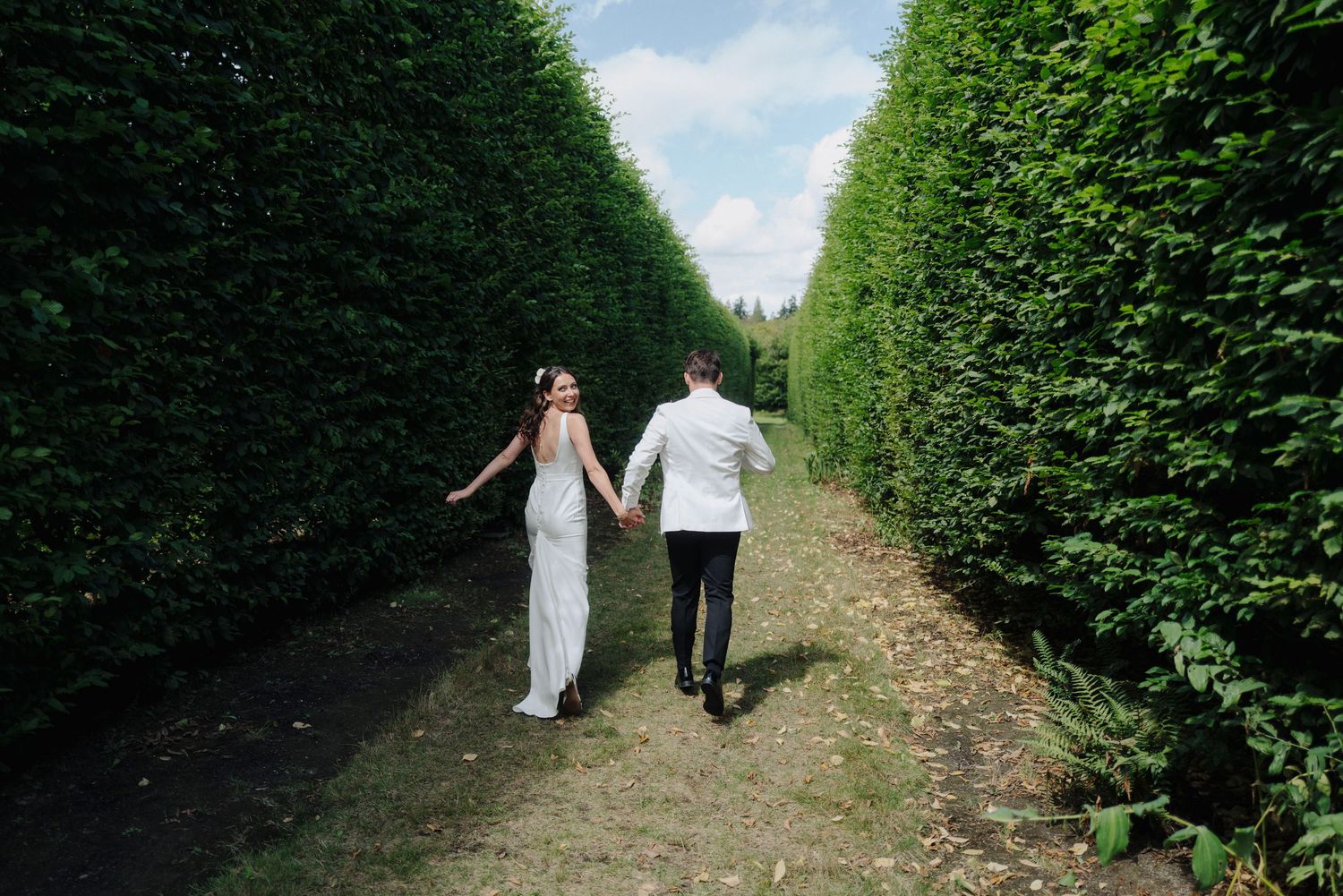 Garden pathway lined with tall hedges creates a romantic wedding photo backdrop.