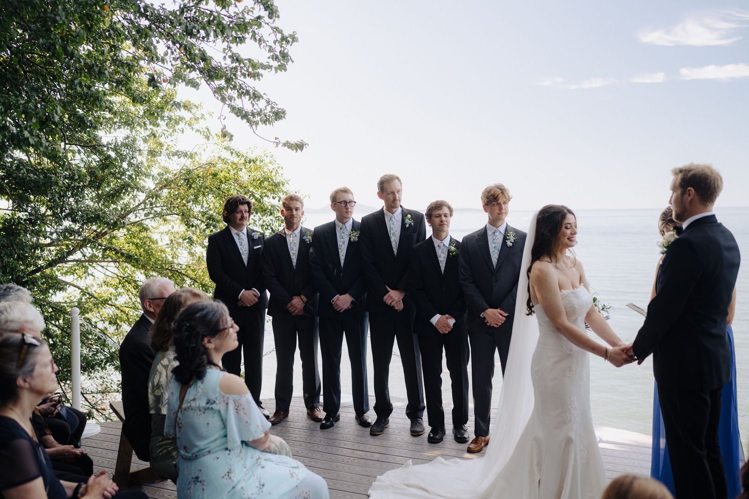 Wedding party lined up on a scenic waterfront deck during the ceremony.