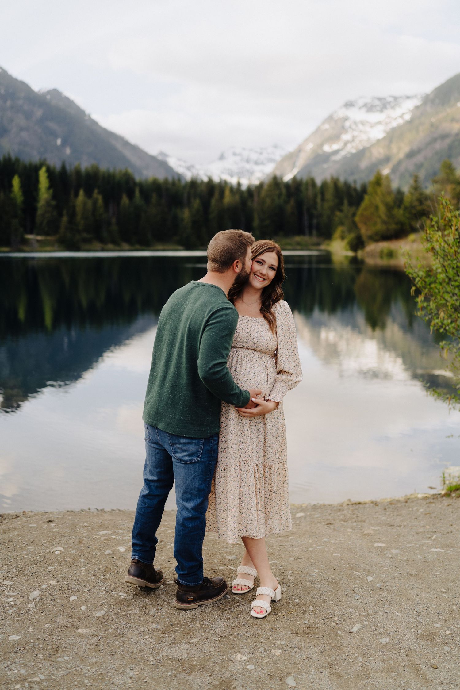 Romantic moment captured on rocky lakeshore with mountain backdrop and evergreen forest.