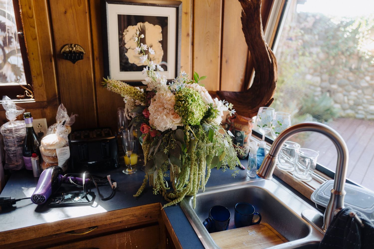 Floral arrangement in a vase next to a sink with rustic wooden paneled walls.