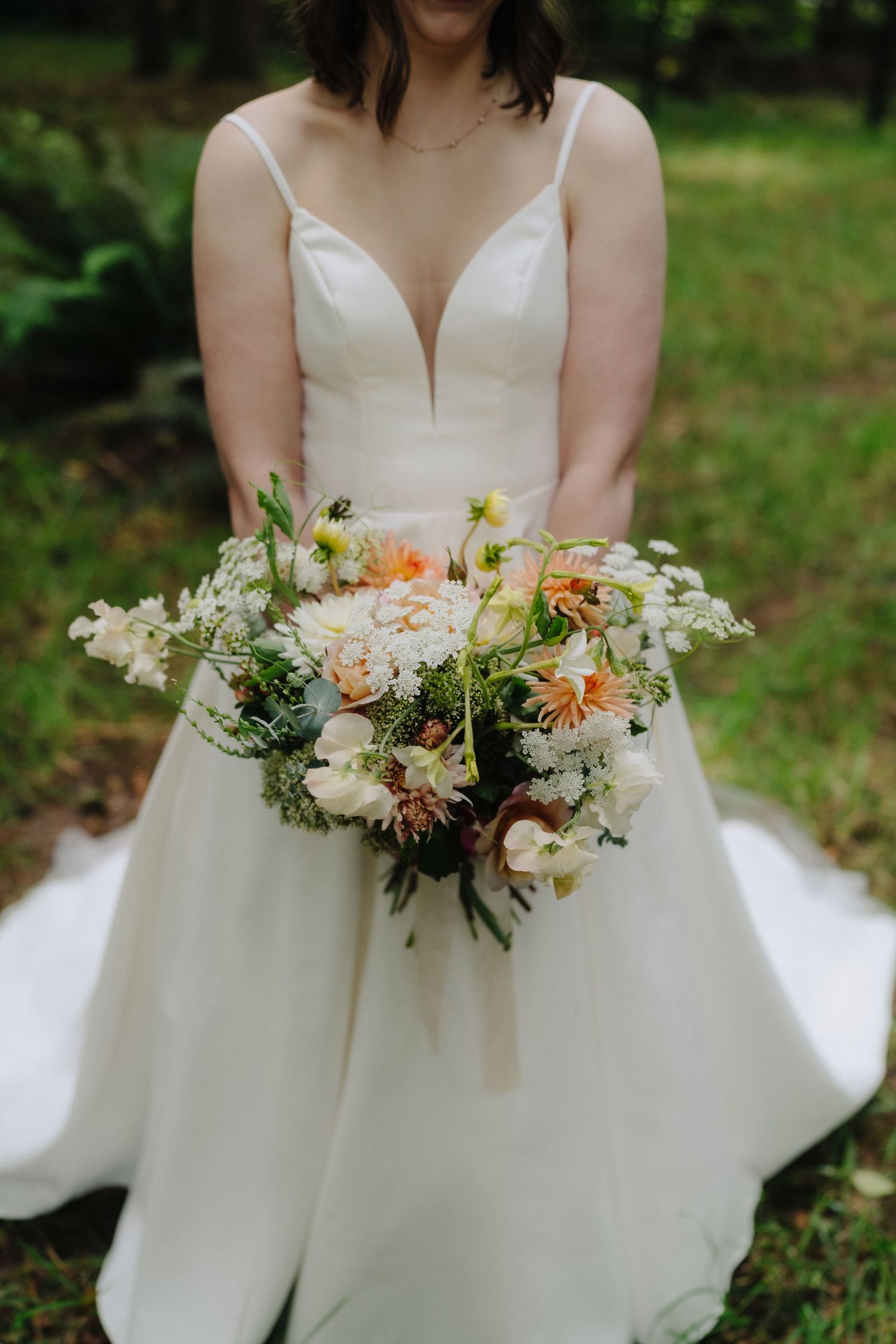 A stunning white wedding bouquet with peach and cream flowers held against an elegant bridal gown in an outdoor setting.