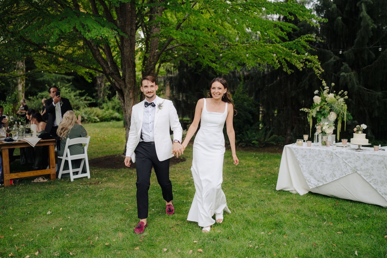 Outdoor wedding reception setup with white tents and tables on a grassy lawn.