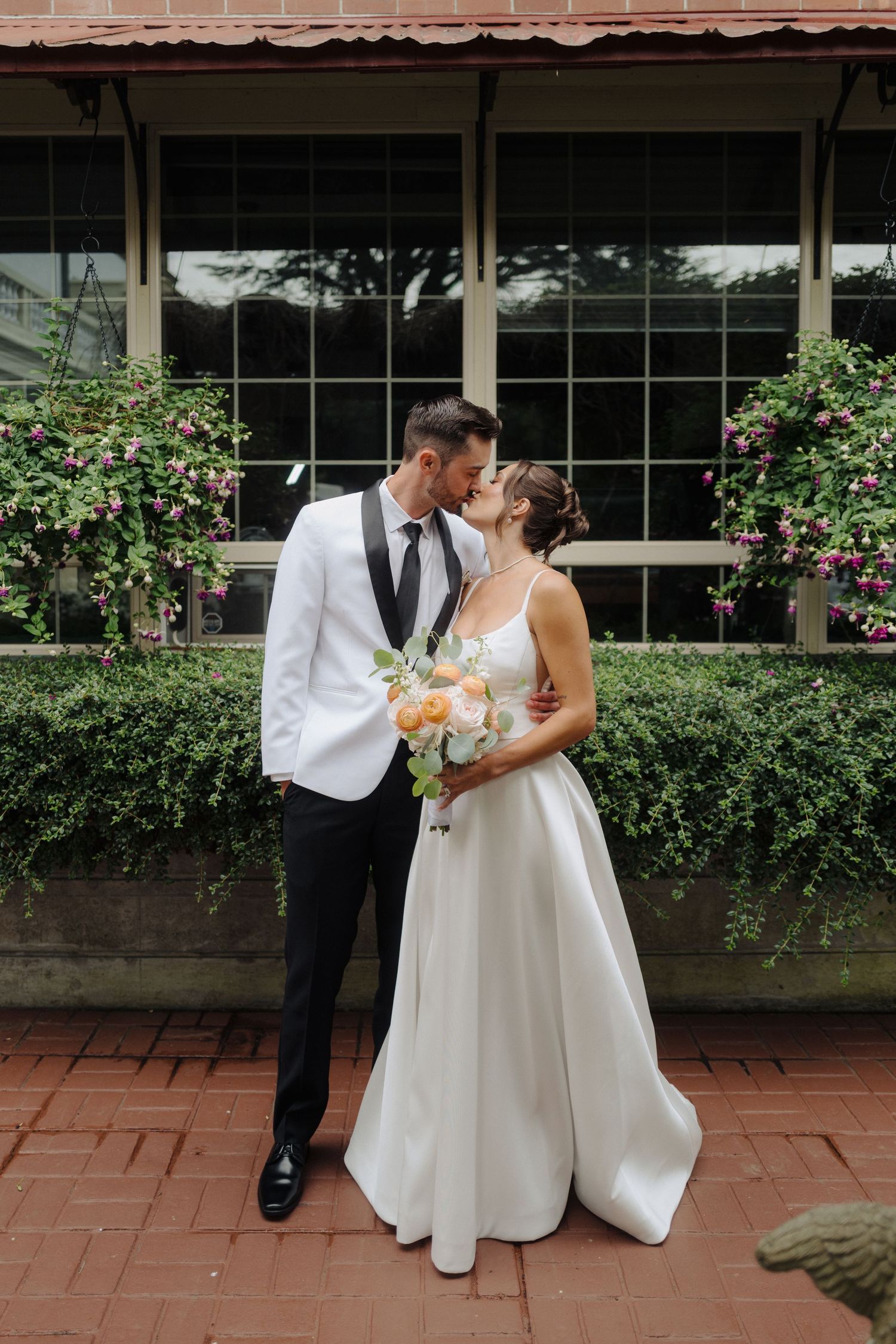 Romantic wedding couple sharing a moment in front of a window with flowering bushes.