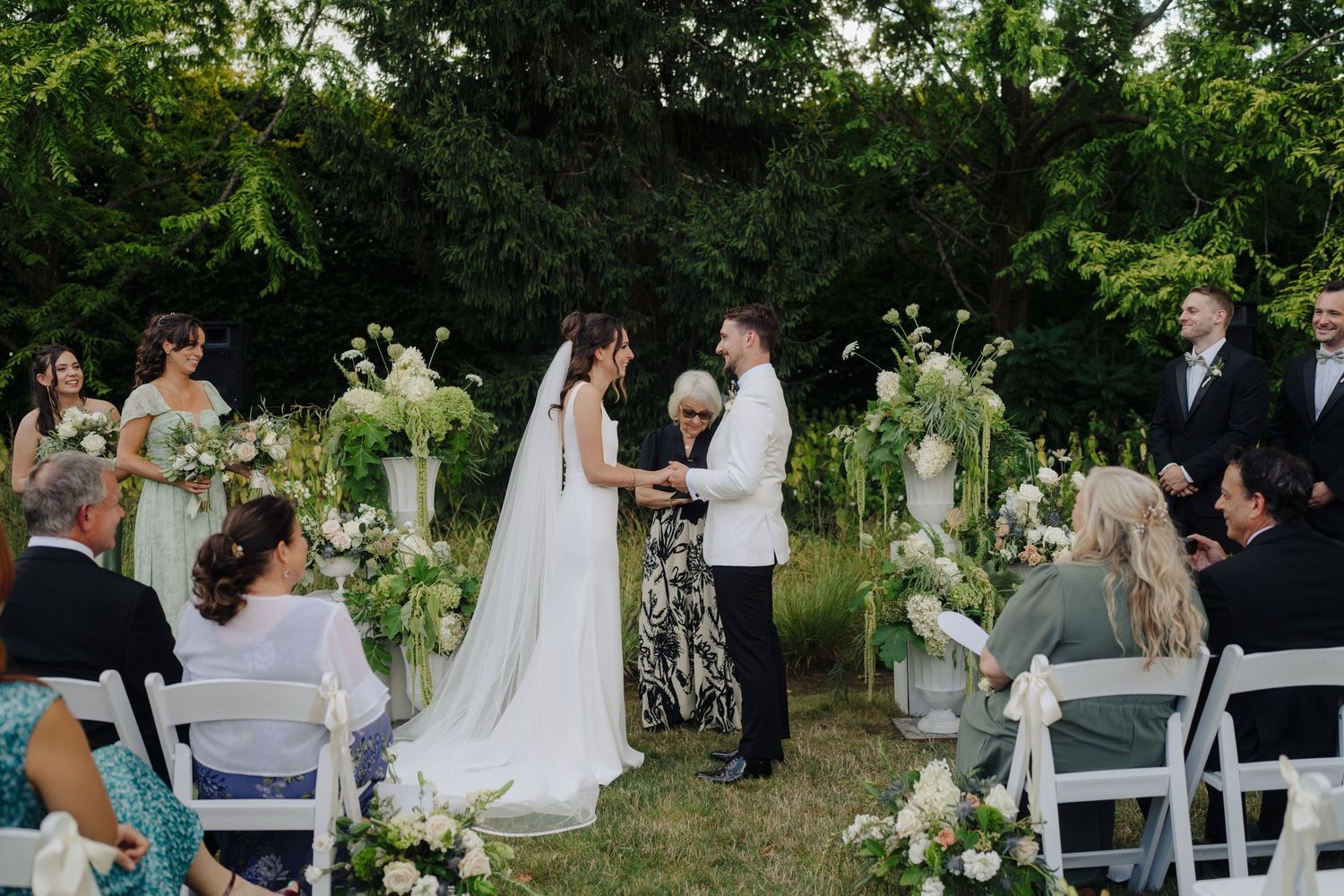 Garden wedding ceremony setup with white chairs and floral arrangements along the aisle.