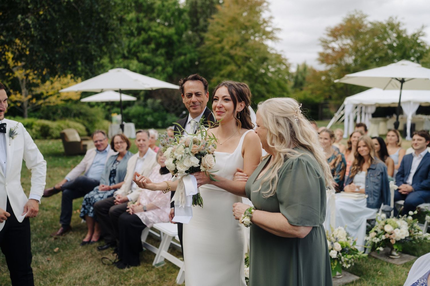Outdoor wedding reception with white umbrellas and guests gathered in a garden setting.
