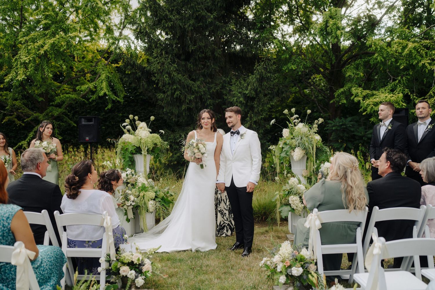Wedding guests gathered on lawn chairs during an outdoor garden ceremony.