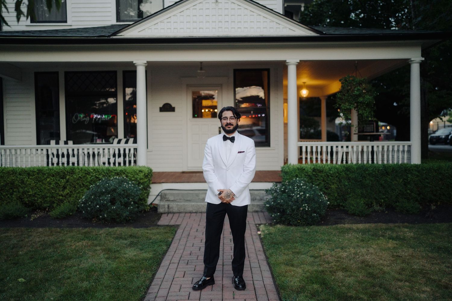 Elegant couple photographed in front of classic white porch with brick walkway.