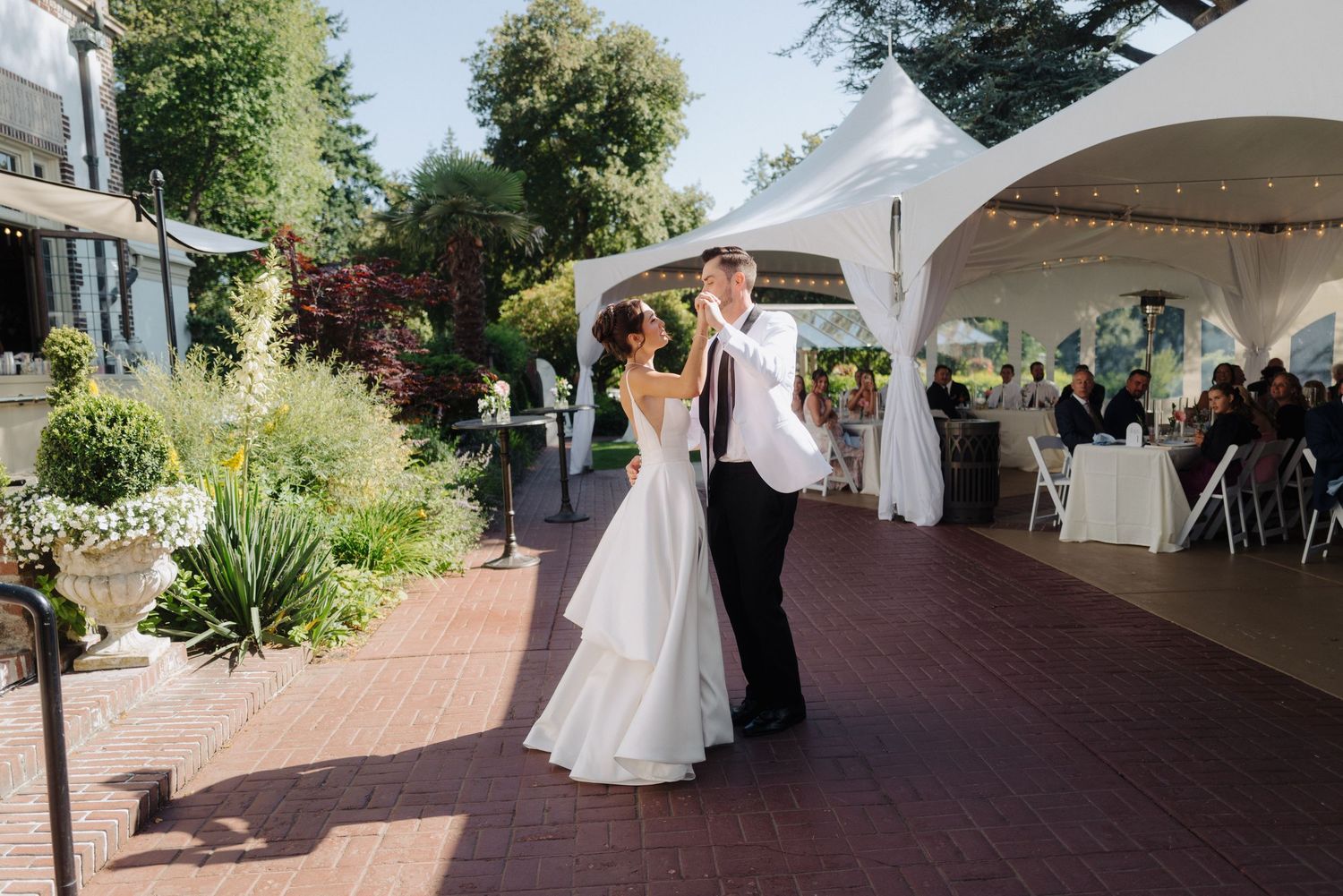 Outdoor wedding venue with white tent and brick pathway surrounded by lush greenery.