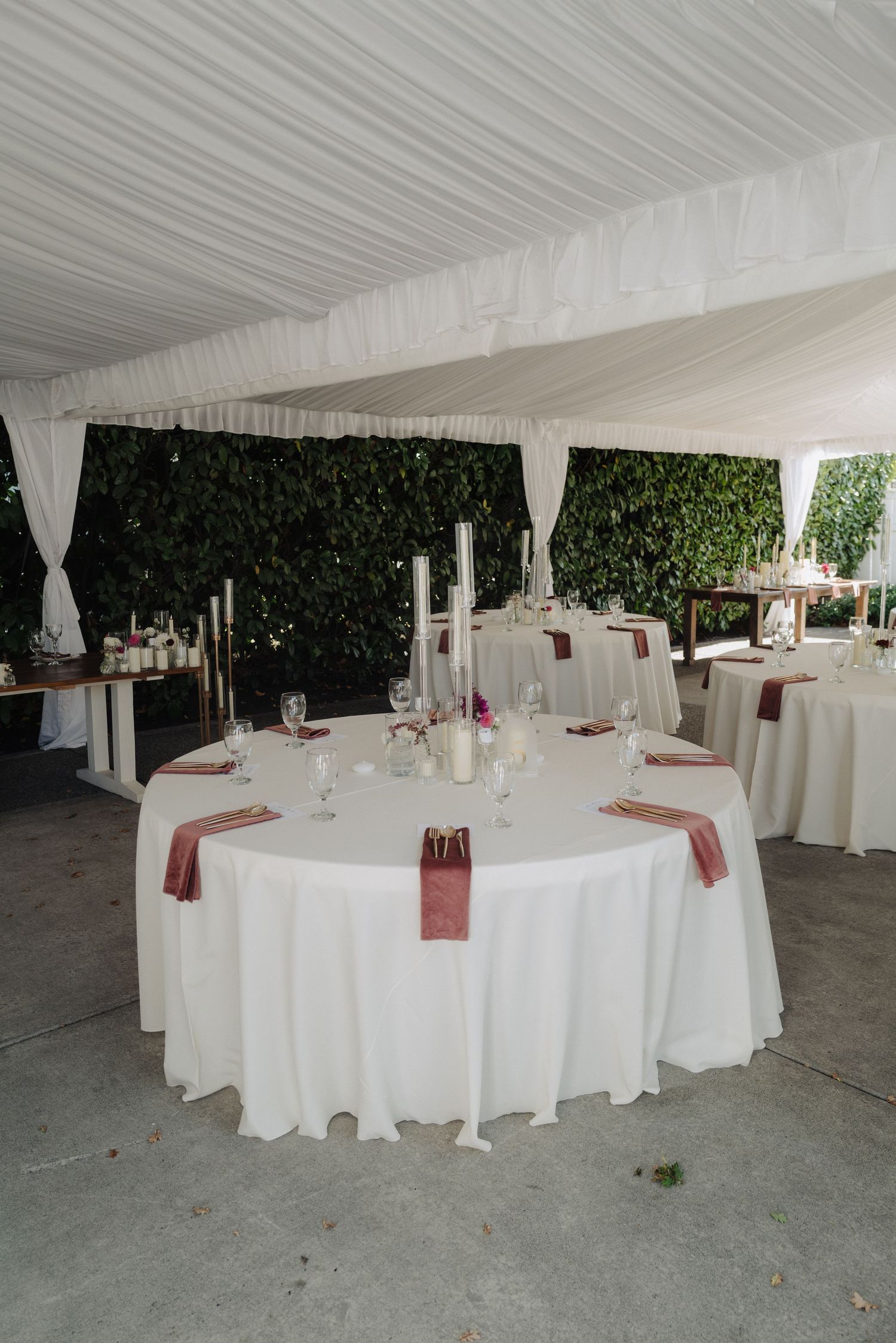 White reception tables set under an elegant tent with burgundy accents and white linens.