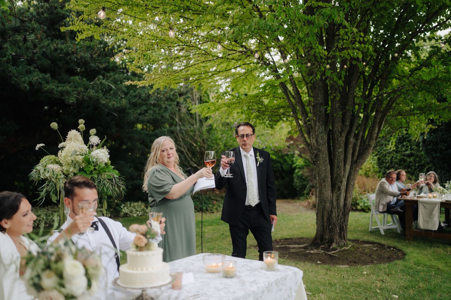 Elegant outdoor wedding reception setup with white tables and chairs under garden trees.