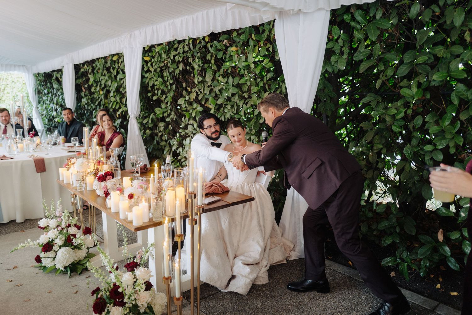 Romantic outdoor reception setup with white tent, candlelight, and ivy-covered walls.