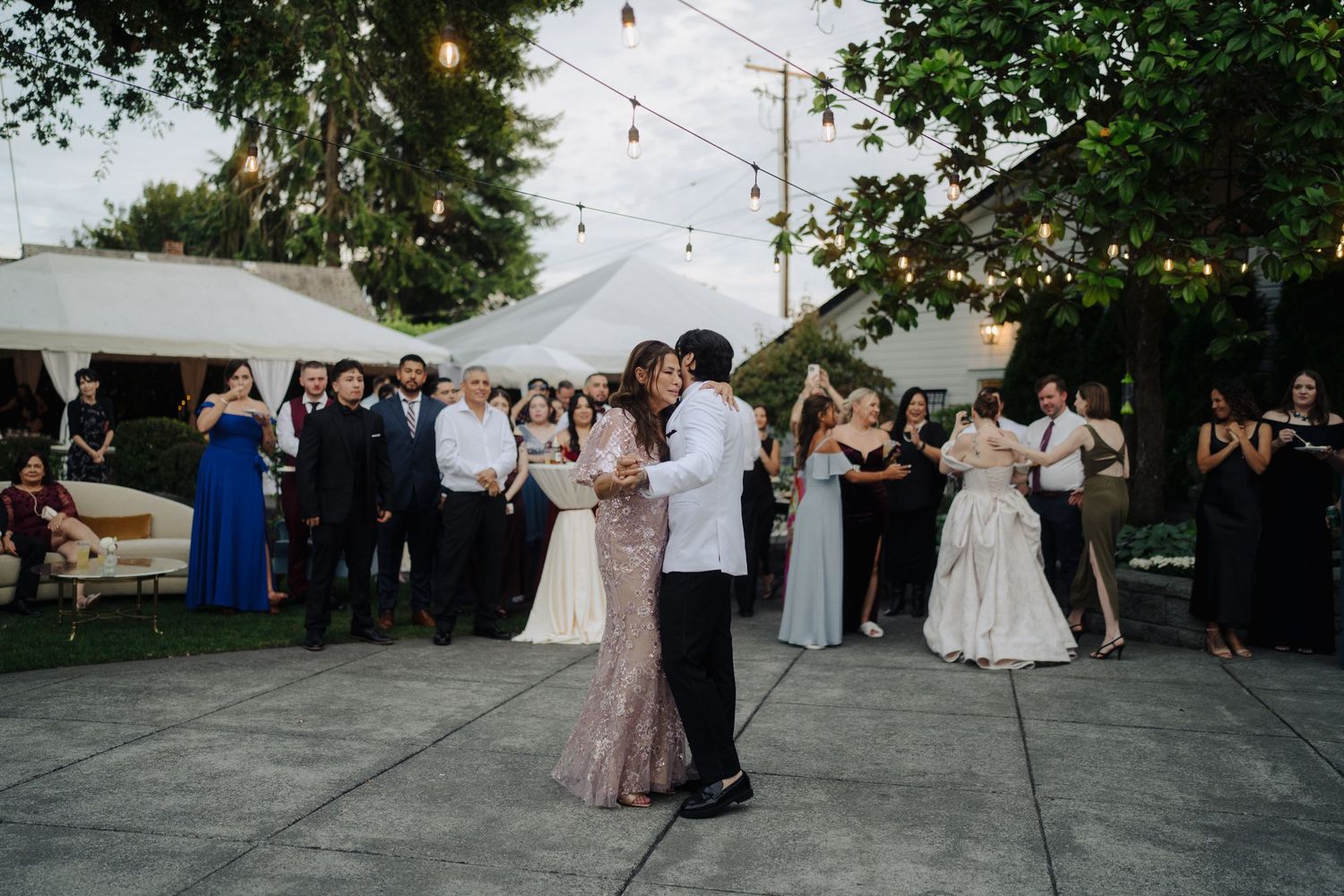 Evening outdoor wedding reception with couples dancing under string lights.