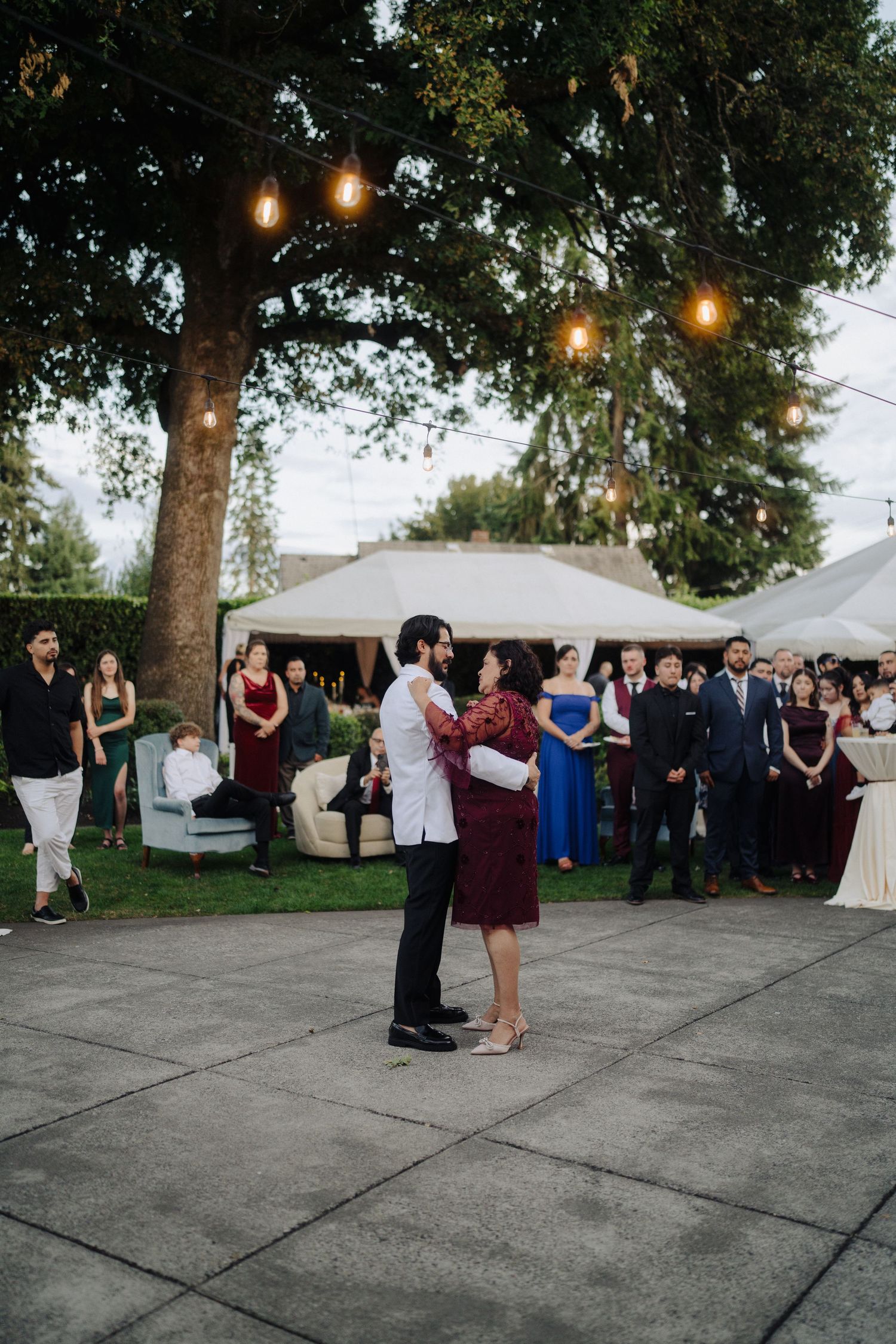 A couple dancing under string lights at an outdoor evening reception.