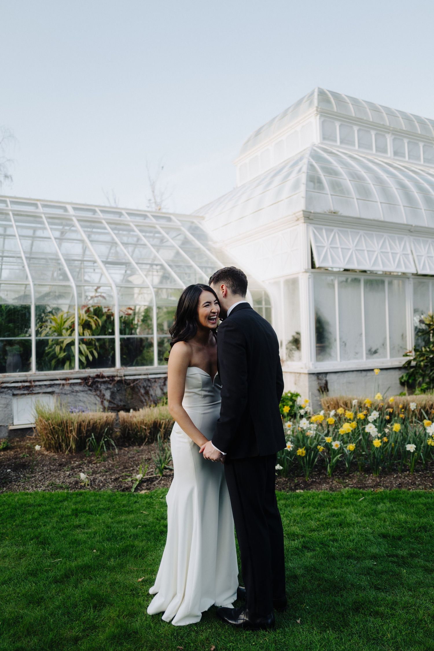 A couple embraces in front of a white conservatory surrounded by spring tulips.
