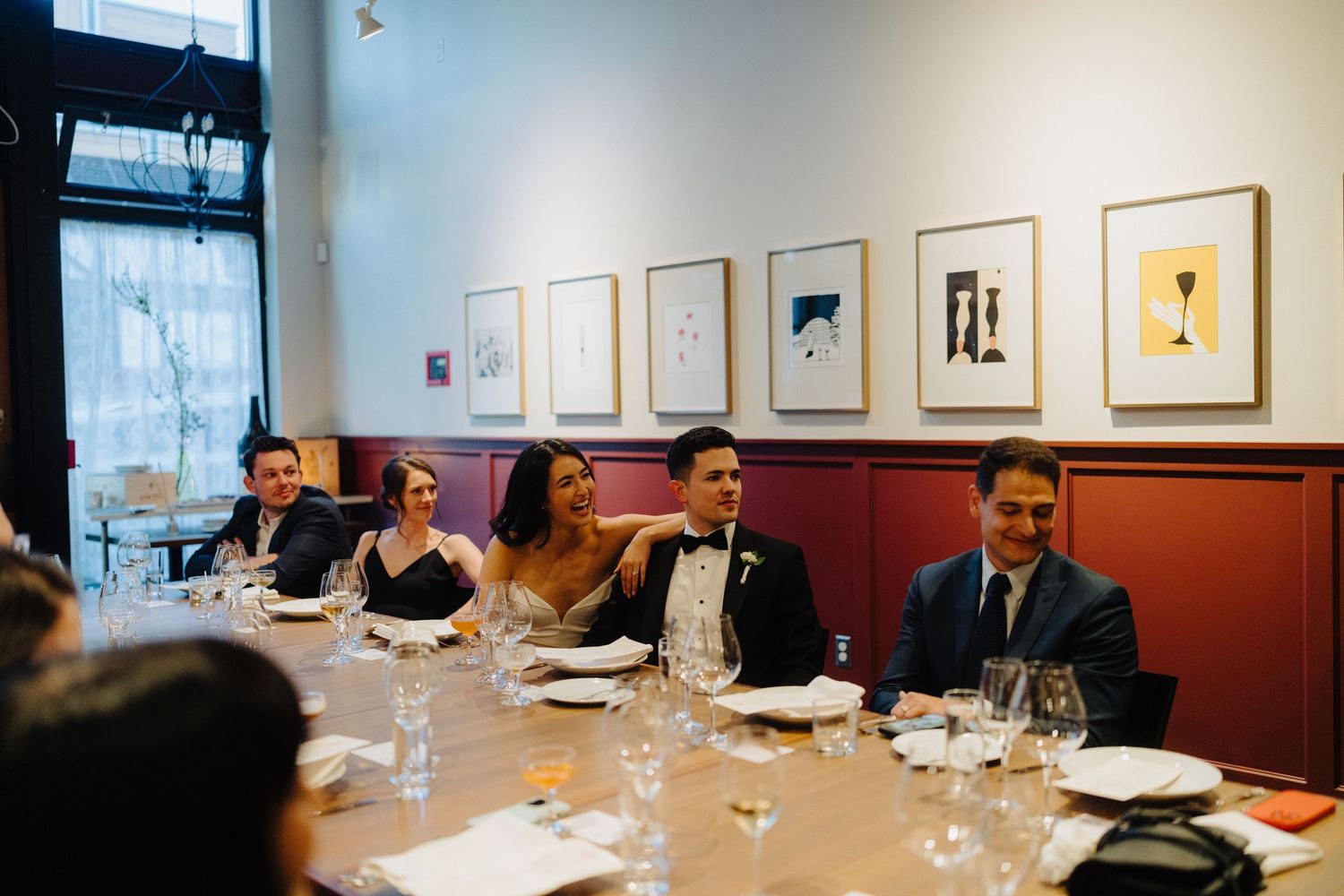 Wedding guests enjoying dinner at an elegant restaurant with framed artwork displayed on the walls.