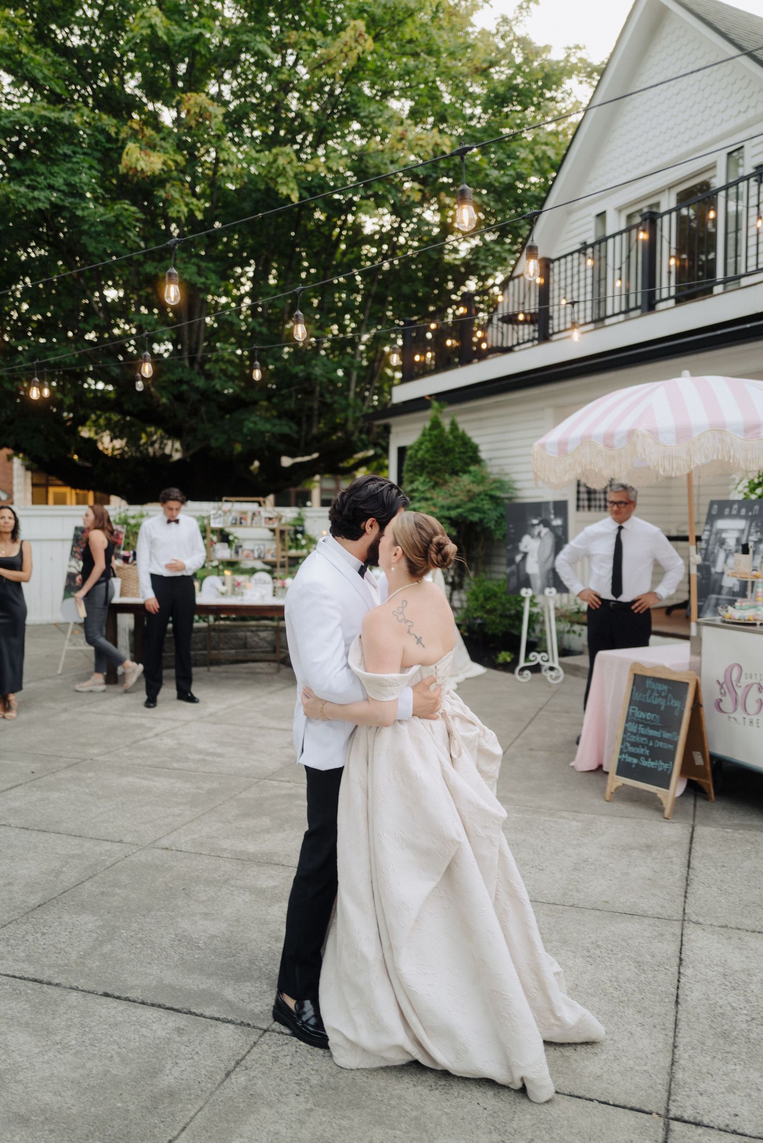 Wedding celebration on an outdoor patio with string lights and white decor.