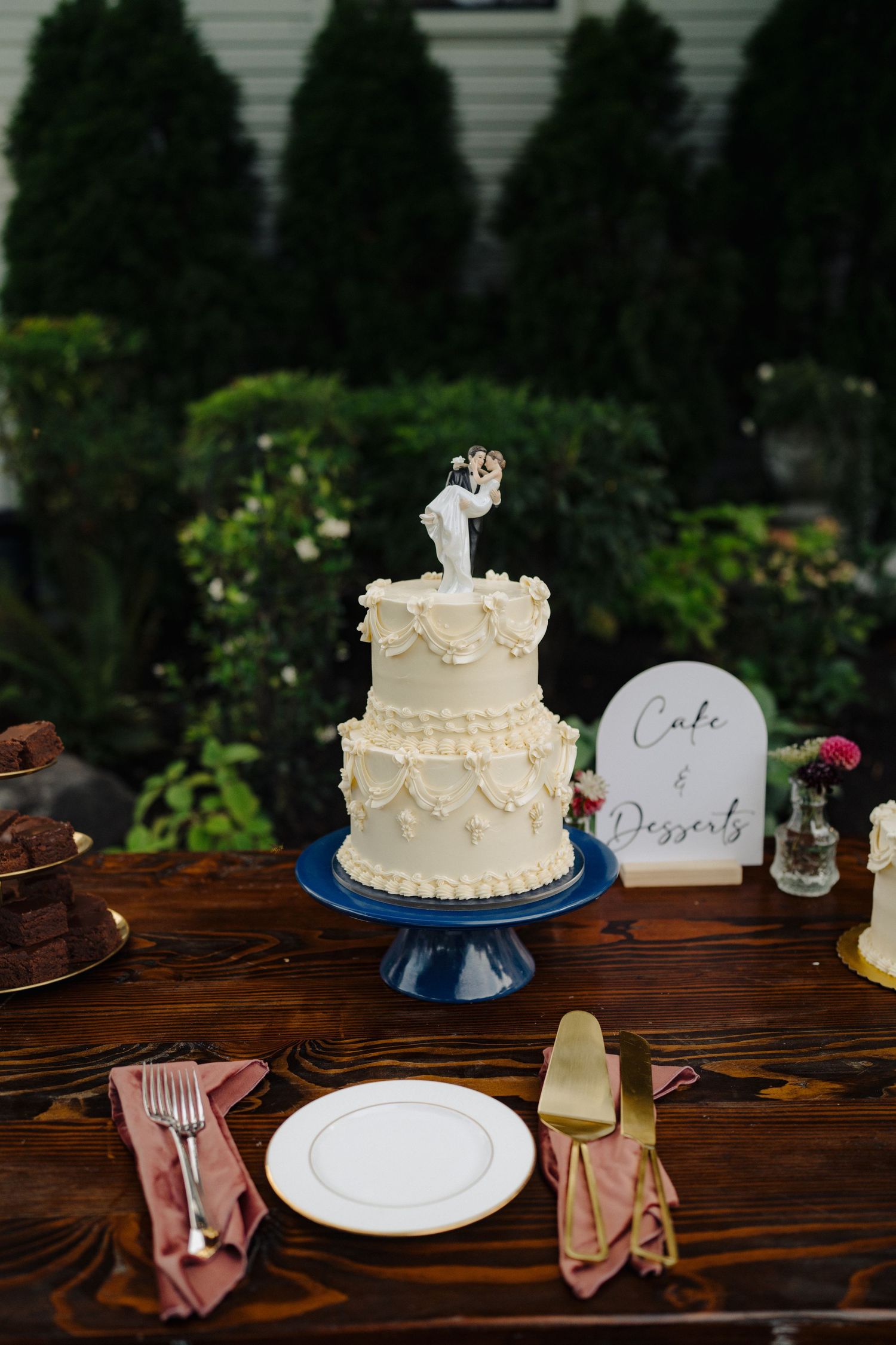 Two-tiered white wedding cake with traditional bride and groom topper on blue cake stand.