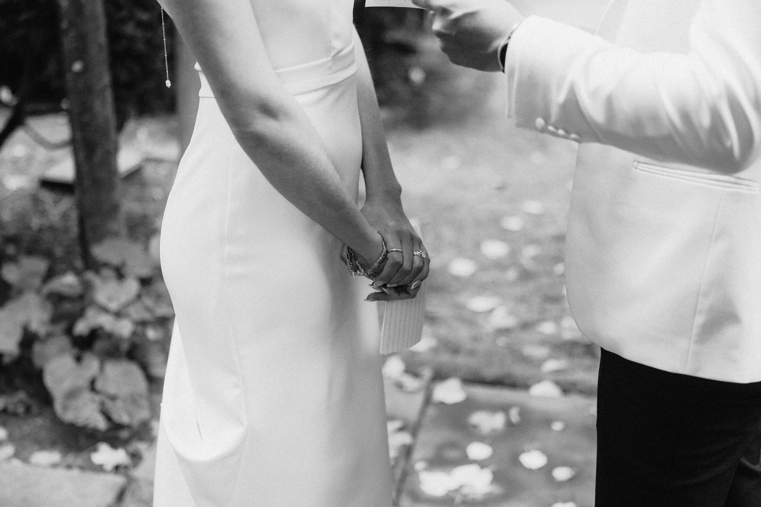 Black and white photo showing hands clasped together during an outdoor wedding ceremony.