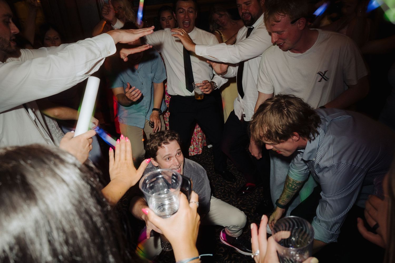 Energetic crowd dancing and celebrating at a dimly lit party or reception.