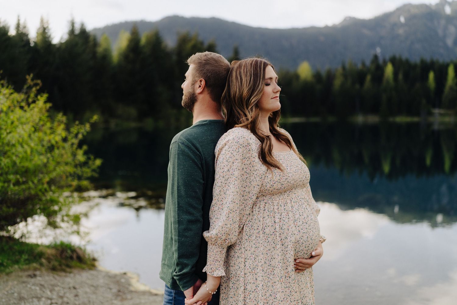 Couple shares intimate moment along shoreline of mountain lake with snow-capped peaks in distance.