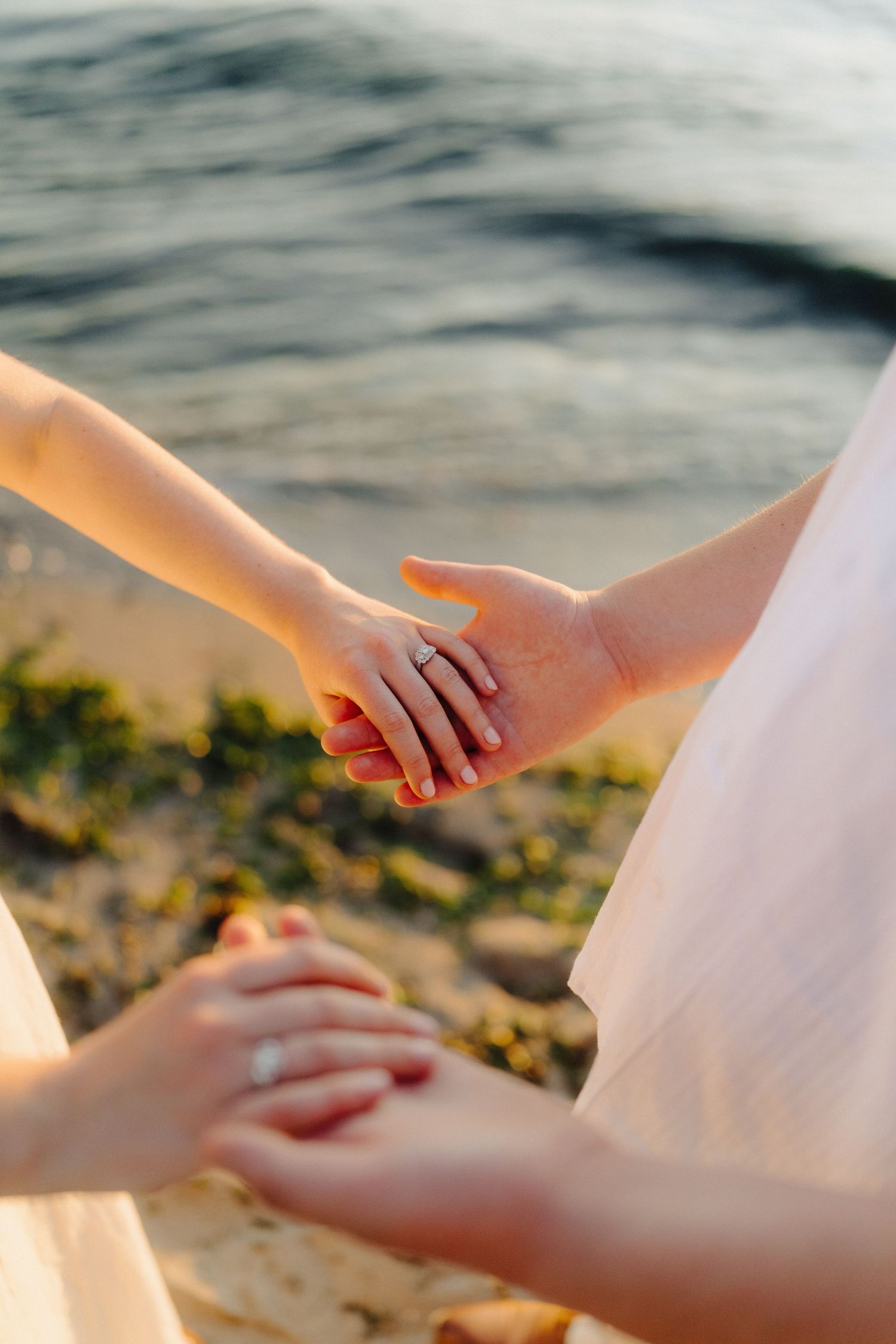 Close-up of hands gently touching on a beach during golden hour with soft natural lighting.