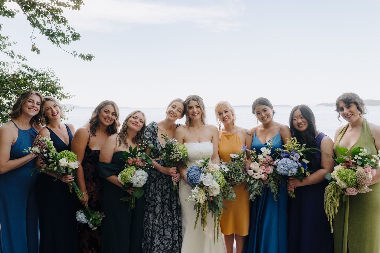 Wedding party in coordinating dresses poses together outdoors.