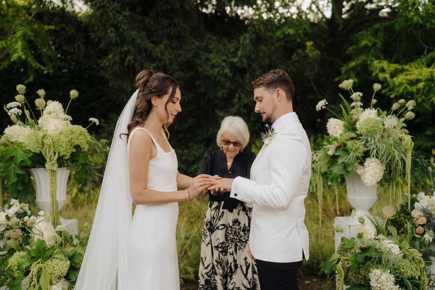 Wedding ceremony in a garden setting with white hydrangea arrangements and natural greenery.